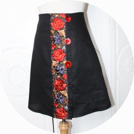 Jupe courte trapeze style portefeuille en lin noir léger et galon en soie brodé de fleurs rouges et bleues